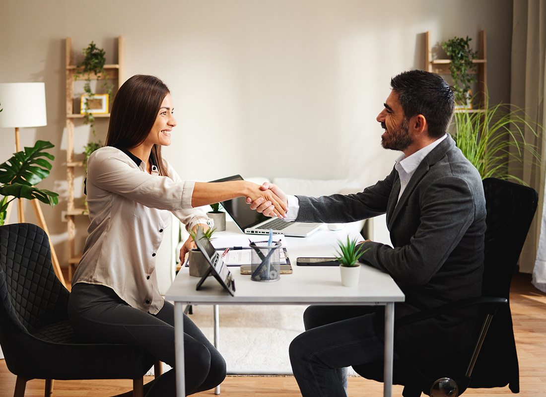 About Our Agency - View of a Smiling Middle Aged Agent Shaking Hands with a Female Client During a Meeting in the Office